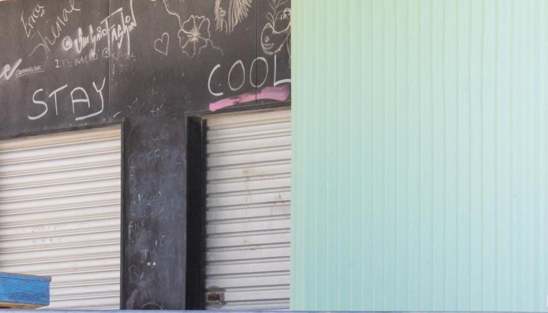 Photograph: Behind a blue wall, is a black wall with two garage doors. Above the doors is graffiti including the words 'STAY COOL' in upper case.